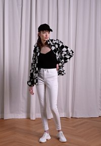 Jaqueta de polar xadrez em preto e branco sobre uma blusa preta, combinada com jeans skinny brancos e ténis brancos; em frente a um fundo suave.