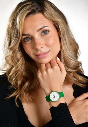 Grüne Silikon-Uhr mit einem runden weißen Zifferblatt, kräftigen schwarzen Zahlen und einer silbernen Lünette, getragen an einem Handgelenk mit einem schwarzen Oberteil.