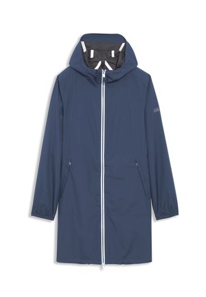 Mand iført en blå hættejakke med lynlås foran og matchende bukser, kigger til siden, iført en sort kasket med logo.