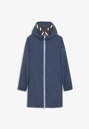 Homme portant un imperméable bleu à capuche avec fermeture éclair à l'avant et pantalon assorti, regardant sur le côté, portant une casquette noire avec un logo.