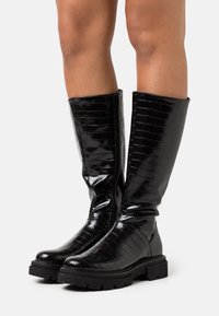 Czarne kozaki do kolan z tłoczonym wzorem w krokodylą skórę, o błyszczącym wykończeniu, solidnej gumowej podeszwie i zamku błyskawicznym z boku dla łatwego zakupu. Teksturowany wzór dla dodatkowych detali.