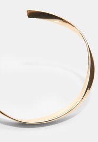 Bracciale a manica in metallo dorato con un design fluido e curvo, caratterizzato da una finitura lucida e un bordo senza soluzione di continuità per un look minimalista.