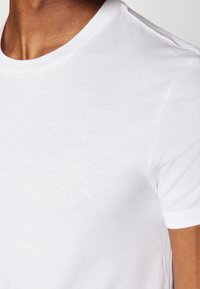 T-shirt blanc à manches courtes en tissu coton lisse avec un col rond et une conception d'épaule sans couture. Apparence minimaliste et légère.