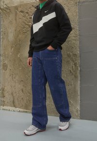 Svart tröja med vit rand, parat med blå jeans med fickor. Outfiten fullända med vita och röda sneakers.