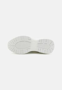 Biała podeszwa sneakersów z teksturowanym wzorem bieżnika, z rowkami i brzegami zapewniającymi trakcję. Gładki materiał gumowy, zaokrąglony kształt.