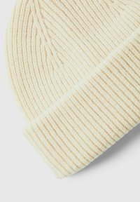 Gorro de punto beige claro con textura acanalada. La tela parece suave y ligeramente difusa, con un borde doblado en la base.