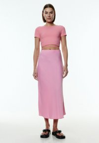 Roze geribbelde crop top met korte mouwen, gecombineerd met een lichtroze, enkel-lange rok met een gladde textuur en eenvoudig ontwerp. Zwarte platform sandalen.