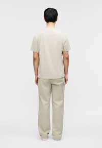 Μπλούζα με κοντά μανίκια σε μπεζ χρώμα με διακριτικό μοτίβο, σε συνδυασμό με ανοιχτό μπεζ παντελόνι. Και τα δύο κομμάτια έχουν άνετη εφαρμογή και μαλακό ύφασμα.