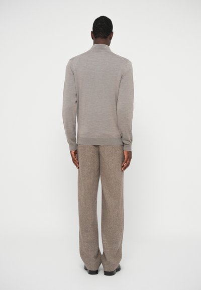 Világosbarna kötött pulóver, állógallérral, széles lábú tweed nadrággal, sötétebb barna árnyalatban párosítva. Simább textúra, testhezálló fazon.