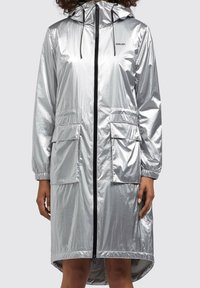 Srebrna wodoodporna kurtka z kapturem, długimi rękawami, dwoma przednimi kieszeniami i czarnym zamek błyskawicznym z przodu. Gładka, błyszcząca tekstura z elastycznymi mankietami.