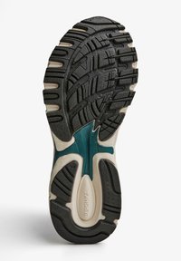 Svart gummisula med strukturerat mönster, med en teal-accent i mellansulan och beige sektioner. Hållbar och designad för grepp.