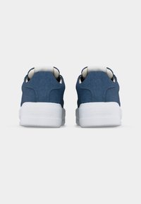 Ζευγάρι μπλε τζιν αθλητικών παπουτσιών με χοντρές λευκές σόλες, εμφανιζόμενα από πίσω σε απλό λευκό φόντο.