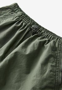 Olivegröna shorts med elastisk midja, som har dragsko-stängning, en jämn textur och subtila sömnadsdetaljer.