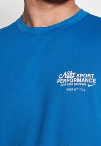 Camiseta de algodón azul royal con cuello redondo, mangas cortas y texto impreso en blanco para la marca y los detalles del producto.