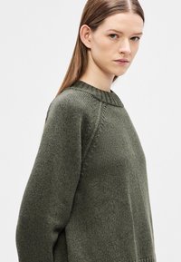 Oliviroheline kudumissärgi ümar kaelus, soonikkoes krae ja laiad, veidi liialdatud varrukad. Sile tekstuur nähtavate kudumismustritega.