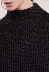 Strickpullover in dunklen Tönen mit hohem Kragen, strukturiertem Muster und einem weichen, groben Material, das über multicolored Flecken verfügt.
