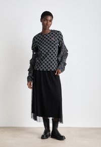 Μαύρη και γκρι ριγέ μπλούζα με μακριά μανίκια και λο�γότυπο NY, φορεμένη πάνω από μια μαύρη πλισέ φούστα, συνδυασμένη με μαύρες μπότες μέχρι τον αστράγαλο.