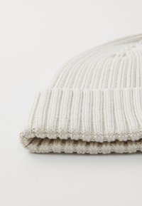 Ribbed knit beanie in light beige, folded cuff design, soft texture, featuring evenly spaced lines created by the knit pattern.
