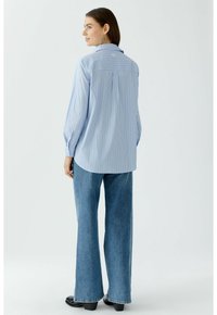 Blue and white striped long-sleeve shirt with a collar, buttoned cuffs, and rounded hem. Paired with wide-leg denim jeans and black shoes.