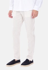 Pantaloni a righe leggeri in beige e bianco, con una vestibilità slim e tessuto testurizzato, abbinati a scarpe espadrillas scure.