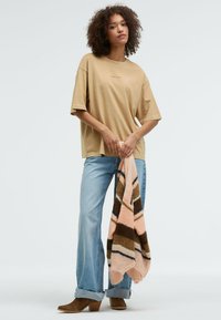 Beige oversized t-shirt with short sleeves, light blue flared jeans, and brown heeled ankle boots. Holding a multicolored striped shawl.
