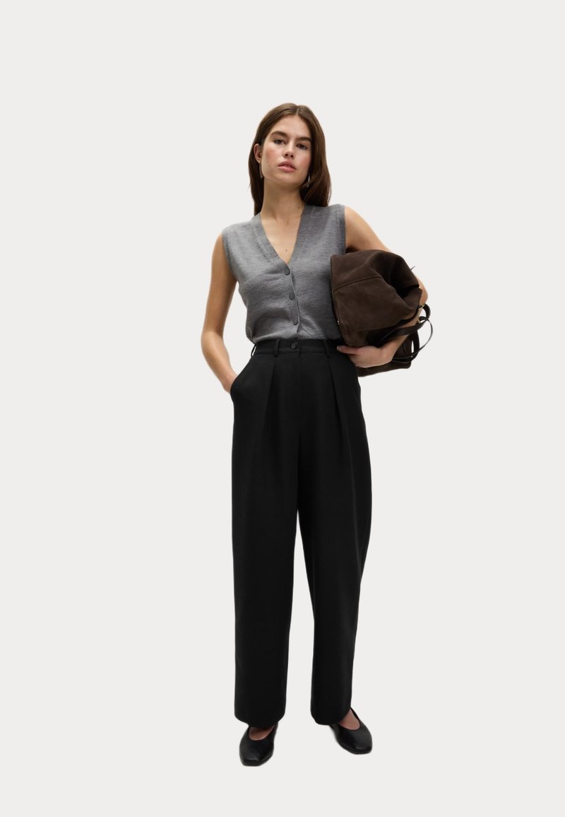 Šedý bezrukávový top s knoflíky, černé kalhoty s vysokým pasem a hnědá surová kabela. Jednoduchý design a neutrální barevná paleta.