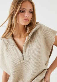 Beige, ribbet strikpullover med halvlukket krave og korte ærmer. Blød tekstur og afslappet pasform, med en v-formet udskæring.