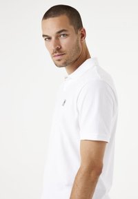 Witte polo met korte mouwen, voorzien van een subtiele logo op de borst, gemaakt van textuur katoen. Eenvoudig, klassiek ontwerp.