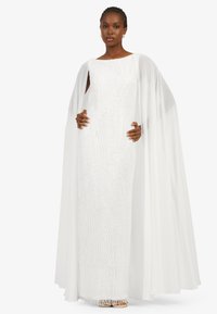White floor-length dress with beadwork and a textured pattern, featuring a flowing cape attached at the shoulders.