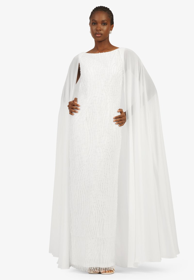 White floor-length dress with beadwork and a textured pattern, featuring a flowing cape attached at the shoulders.