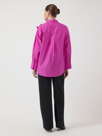 Camisa grande fucsia con cuello, mangas largas y puños con botones; combinada con pantalones de pierna ancha negros. Tejido suave y líneas limpias.