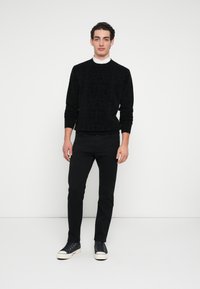 Czarny sweter o fakturowanej powierzchni z okrągłym dekoltem, noszony na czarnych obcisłych spodniach oraz granatowych trampkach z białymi podeszwami. Prosty, monochromatyczny zestaw.