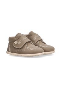 Zapatos marrones para niños pequeños con costuras blancas, correas de Velcro y suelas suaves color beige, mostrados uno al lado del otro sobre un fondo blanco.