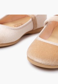 Un paio di scarpe Mary Jane in velluto beige e beige chiaro, piatte, con punte arrotondate e cinturini elastici, su sfondo bianco.