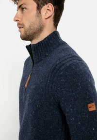 Granatowy sweter wełniany z wysokim żebrowanym kołnierzem, pół-zamkiem oraz teksturowanym wzorem, z skórzaną naszywką na lewym rękawie.