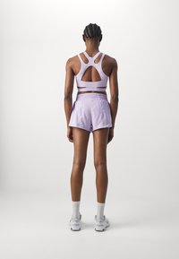 Sujetador deportivo lavanda con diseño de recortes y pantalones cortos a juego. Las telas son suaves. Cuenta con una pretina elástica y detalles de costuras visibles.