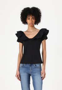 Top nero a maniche corte con scollo a V profondo e dettagli arricciati lungo le spalle, abbinato a jeans in denim azzurro chiaro.