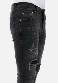 Zwarte denim jeans met een slim fit, voorzien van versleten patches, lichte spatten en metalen hardware op de zakken en tailleband.