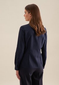Marineblauwe longsleeve shirt met een aansluitend ontwerp, knoopmanchet en gladde stof. De achterkant heeft een centrale naad voor structuur.