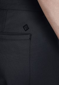 Black pants with a smooth, textured fabric, featuring a rear pocket and a small, embossed logo near the pocket.