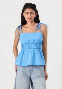 Light blue sleeveless top with adjustable tie straps, gathered waist, and flared hem; made of soft, smooth fabric for comfort.