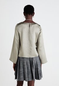 Light green blouse with long, wide sleeves, featuring a back button closure. Worn with a pleated gray skirt. Smooth, slightly textured fabric.