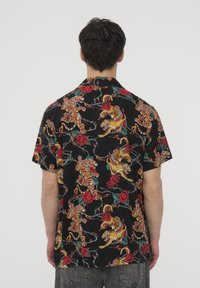 Koszula z krótkim rękawem w czarnym kolorze z żywym wzorem tygrysa w kolorze czerwonym i żółtym, przeplatającym się z zielonymi winoroślami i różami.