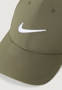 Maslinasto zelena Nike bejzbol kapa s bijelim izvezenim swoosh logotipom sprijeda i zakrivljenim vizirkom.