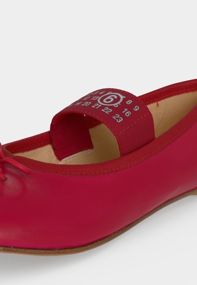 Chaussure de ballet plate rouge avec une bride élastique montrant plusieurs numéros et la taille 6 entourée de blanc sur la bride.