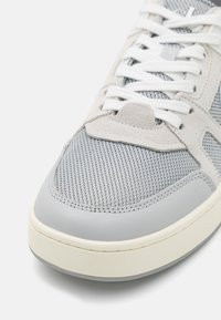 Sneaker grigie con tomaia in mesh e dettagli in suede, punta rotonda e lacci bianchi. Suola spessa in gomma color crema e grigia.