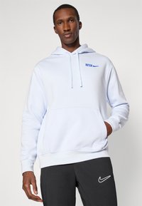 Svetlo modrá mikina s kapucňou a predným vreckom, sťahovacia šnúrka na kapucni a modré logo "INTER" nad znakom Nike. V páre s čiernymi nohavicami.