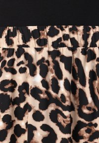 Tissu à motif léopard avec de grandes taches noires et brunes sur un fond beige, présentant une taille froncée et une texture lisse.