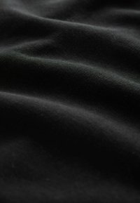 Schwarzer Stoff mit einer glatten, matten Textur, der subtile Falten und Täler aufweist. Die Oberfläche ist einheitlich und ohne Muster oder erhabene Details.