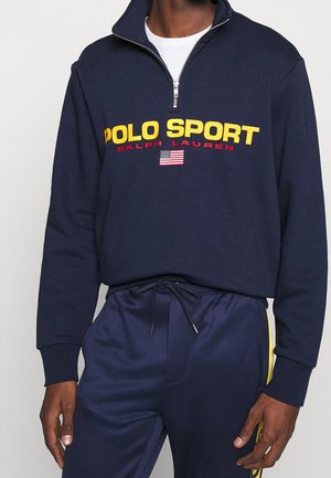 Marineblauwe quarter-zip sweatshirt met gele "POLO SPORT" tekst, rode "RALPH LAUREN" tekst en een kleine Amerikaanse vlag boven marineblauwe sweatpants met gele streep en trekkoord.